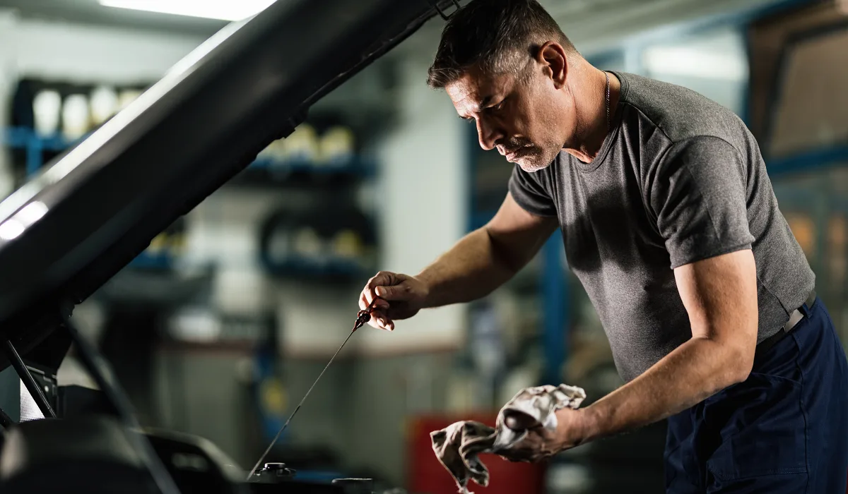 Prevenir el desgaste prematuro del motor de arranque: Hombre checando el aceite del motor del auto